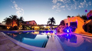 Una piscina con borde de baldosas, palmeras y un edificio con fachada iluminada.