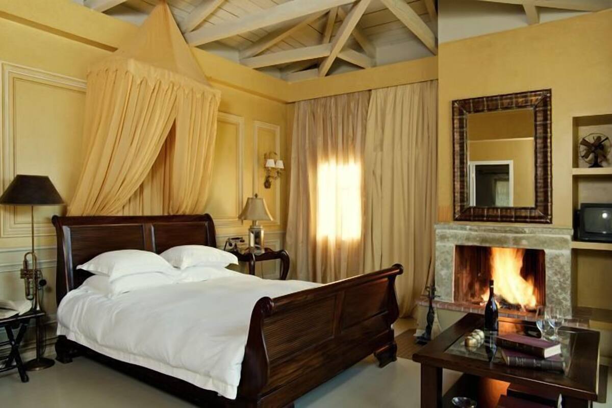 Un dormitorio tradicional con una cama de madera, una chimenea, un espejo y una mesita de noche.