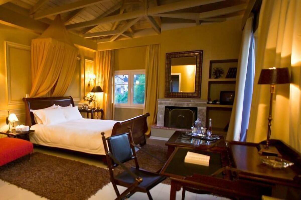 Una habitación de hotel con cama, escritorio, sillón, chimenea y un espejo grande.