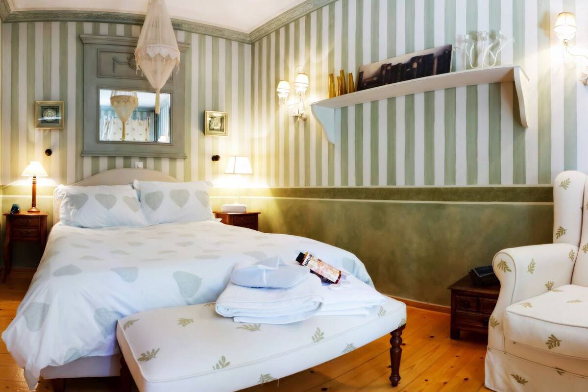 Una habitación de hotel con una cama grande, mesitas de noche, una silla, un estante con libros y una araña.