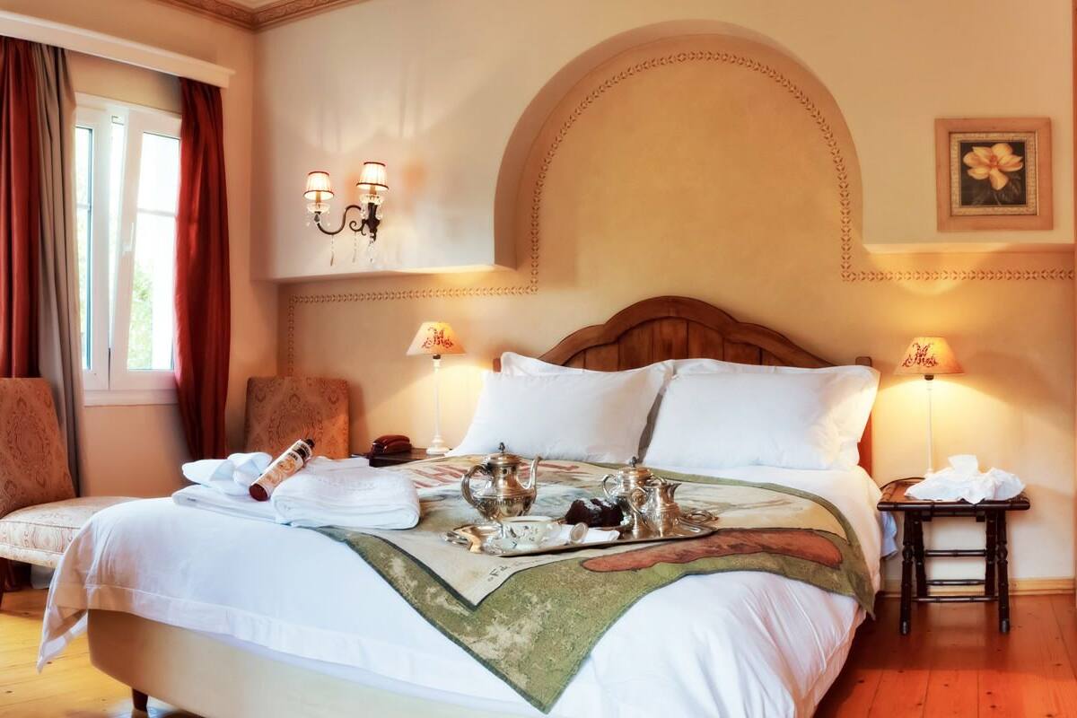 Habitación de hotel con una cama grande, dos lámparas de noche, un cabecero de madera y una mesita con lámpara.