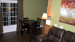 Ein Wohnzimmer mit Ledersofa, einem Esstisch mit Stühlen, einer Lampe und einem Gemälde an der Wand.