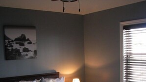 Ein ordentlich bezogenes Bett mit einem gemusterten Überwurf, einer Nachttischlampe und einem Deckenventilator.