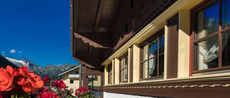 Ein traditionelles Chalet mit Holzhülle, grossen Fenstern und einem Balkon mit Blick auf einen Garten mit roten Blumen.