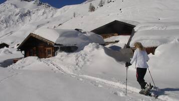 A wooden cabin with a snow-covered roof, surrounded by a snowy mountain landscape.