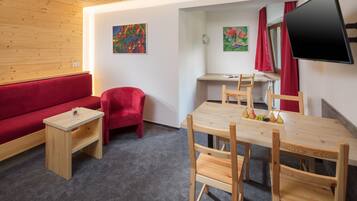 Ein Zimmer mit einer roten Couch, einem kleinen Holztisch, einem Holzbüro mit Stuhl und einem an der Wand montierten Fernseher.