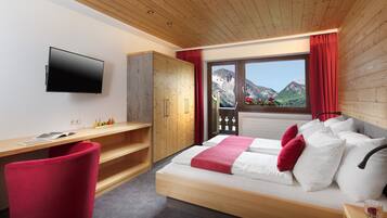 Un dormitorio moderno con techo de madera, una cama con ropa de cama blanca y roja, un televisor montado en la pared y una ventana con vistas a la montaña.