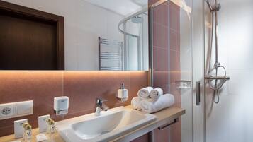 A modern bathroom with a large sink, a glass-enclosed shower, and neatly rolled towels on the counter.