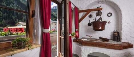 Una habitación con un banco de madera, una olla colgante y un ventanal con cortinas rojas.