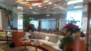 A modern lounge area with a curved sofa, round tables, and potted plants. - Hotel Zurigo (Rimini)