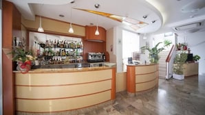 A bar area with a curved counter, hanging pendant lights, and a variety of bottles. - Hotel Zurigo (Rimini)