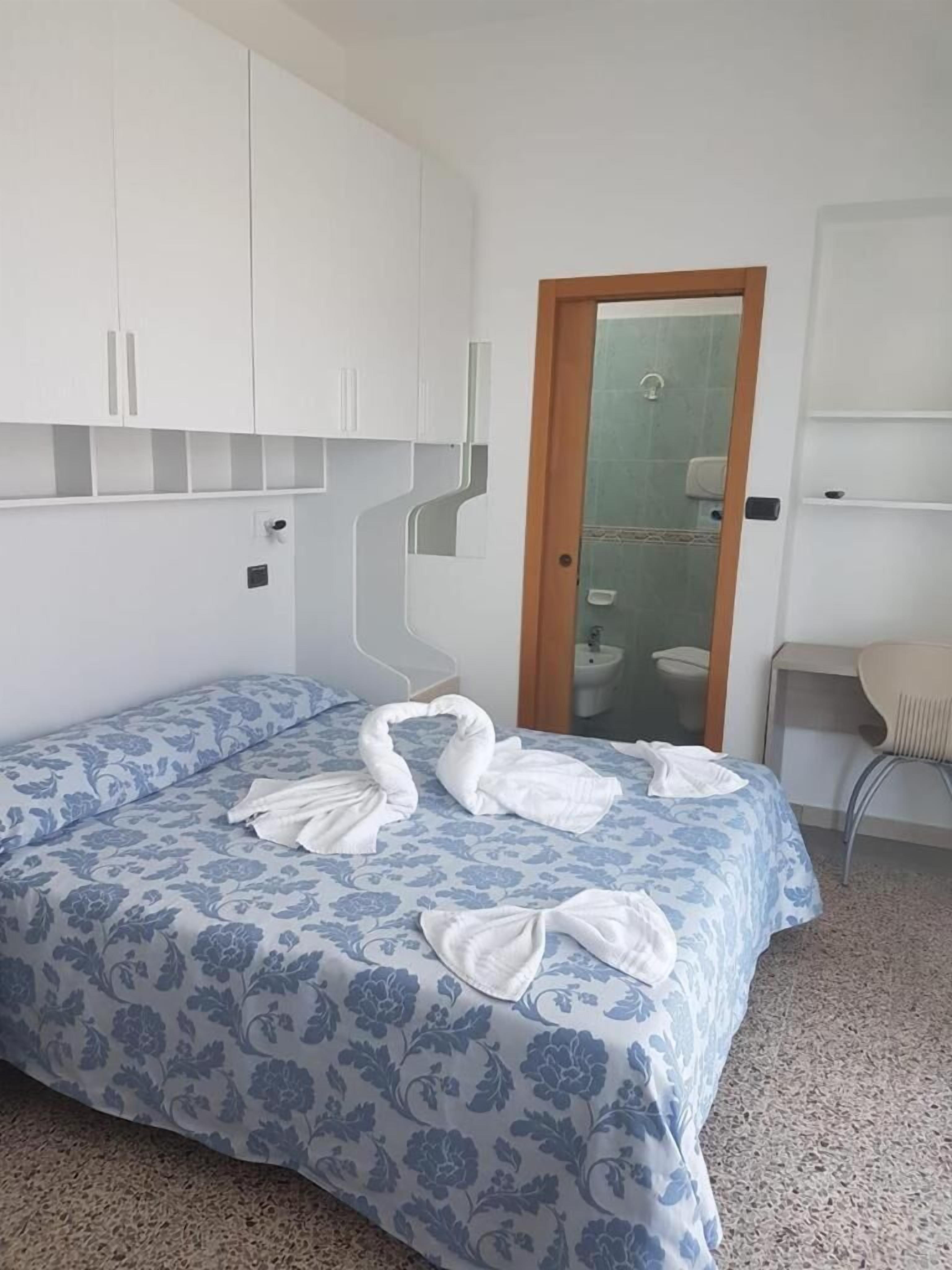 A bedroom with a bed, white wardrobe, and a bathroom visible through a glass door.