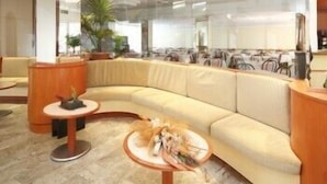 A modern hotel lobby with a curved sofa, a reception desk, and a decorative centerpiece on a round table. - Hotel Zurigo (Rimini)