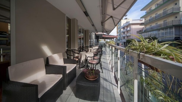 A balcony with wicker furniture, a table, and potted plants. - Hotel Zurigo (Rimini)