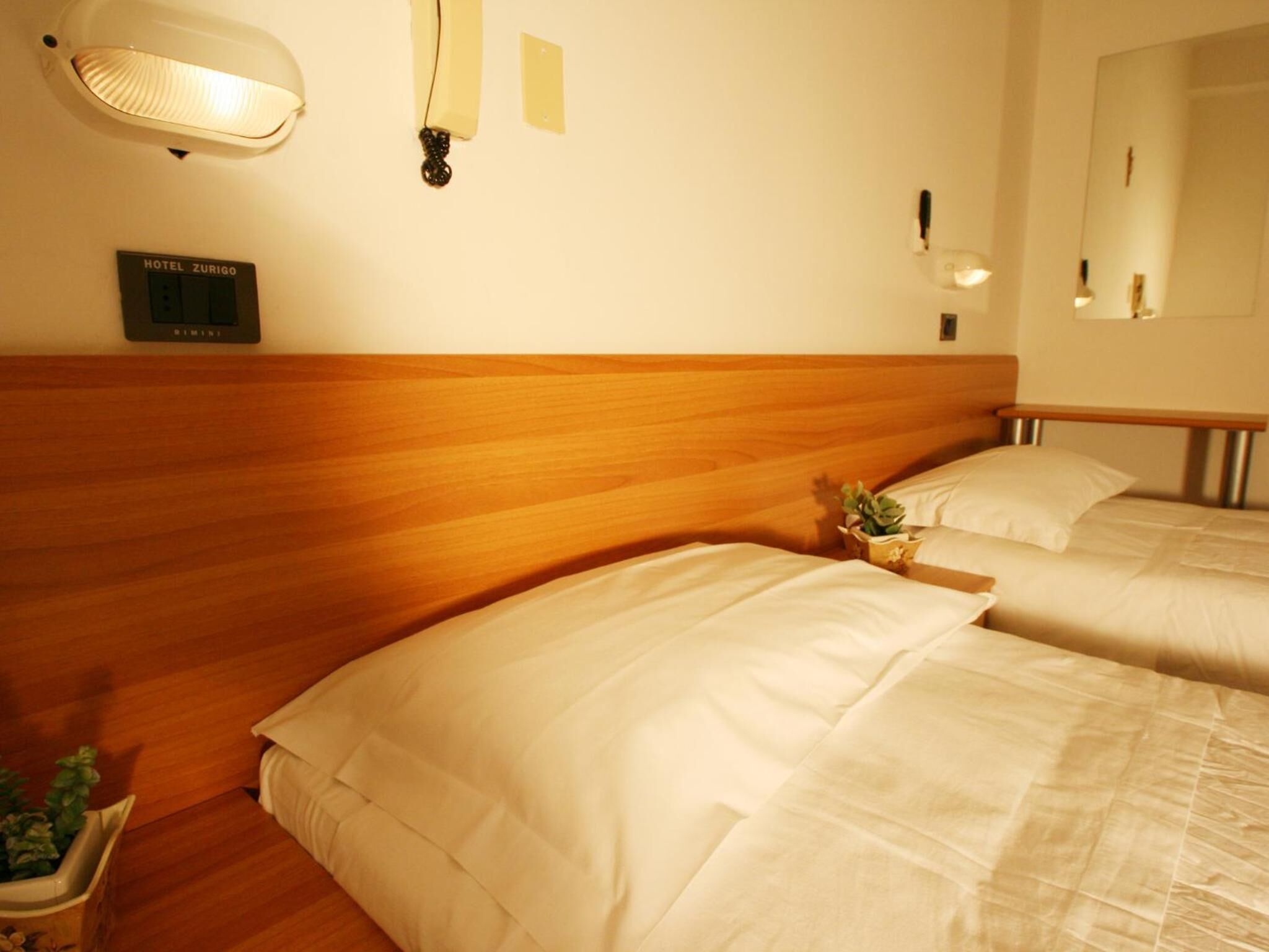 A hotel room with two beds, a wooden headboard, a wall-mounted light, and a sign indicating the hotel name.