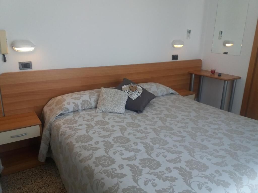 Ein Schlafzimmer mit einem Holzkopfteil, einer zudeckenden Bettdecke mit Blumenmuster, zwei Nachttischen mit Lampen und einem kleinen Nachttisch mit einer Tasse.