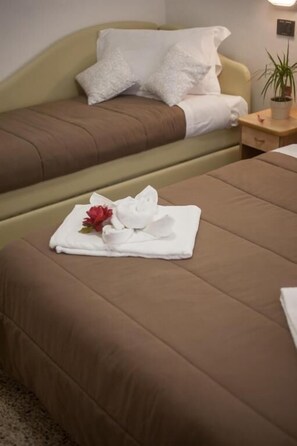 A hotel room with two beds, a nightstand with a plant, and a neatly made bed with a towel and flower. - Hotel Zurigo (Rimini)