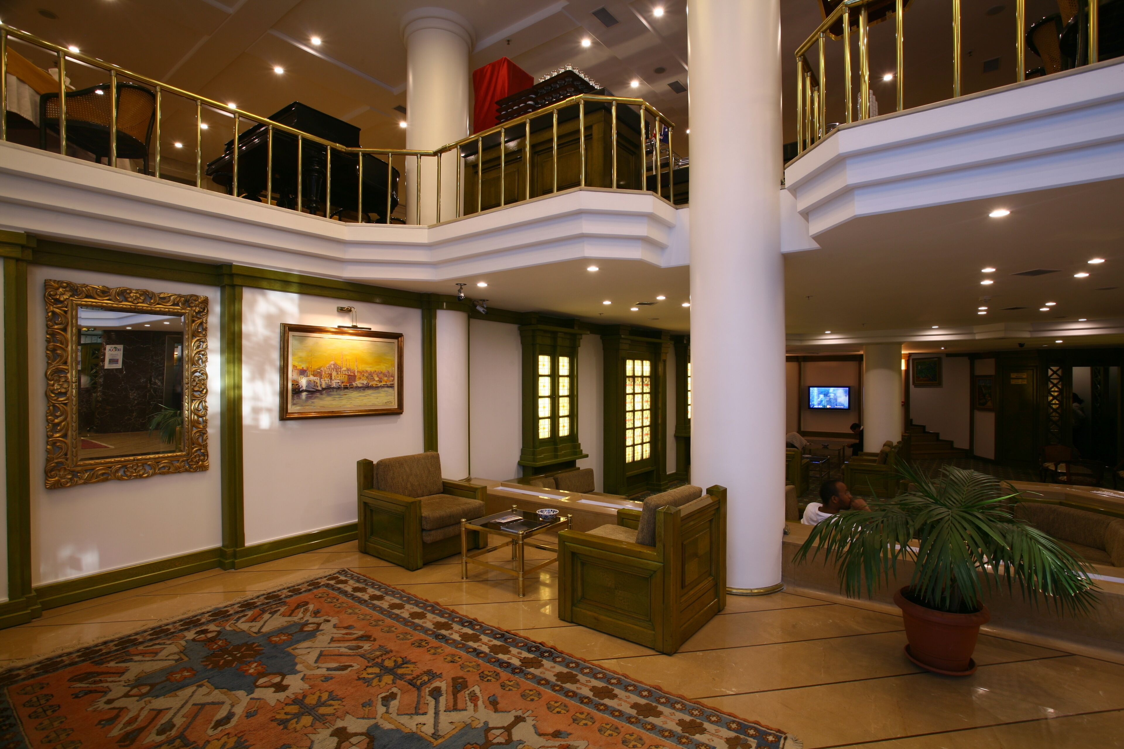 A spacious lobby with a high ceiling, a piano, a large painting, and a television on a wall.