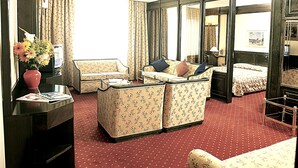 Habitación de hotel con sofá, una pequeña mesa con un florero, una cama con cubrecama estampado y un ventanal con cortinas.