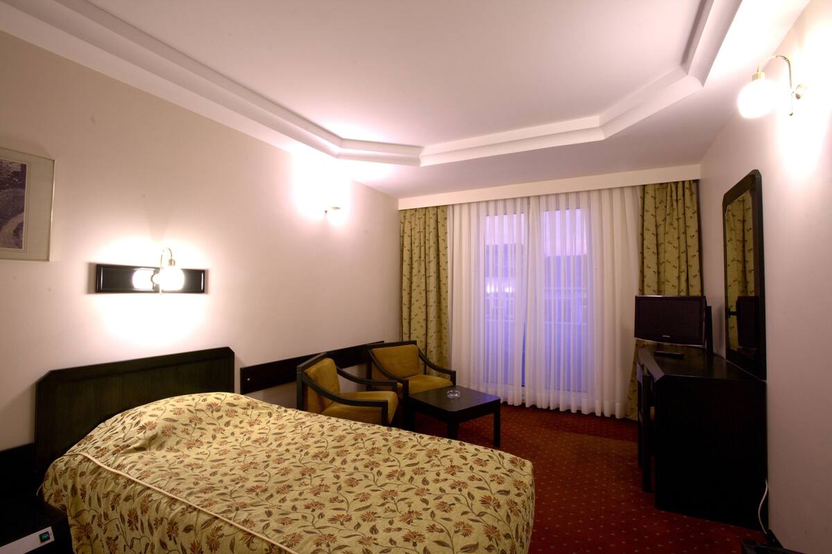 Habitación de hotel con cama, escritorio, silla, televisión y ventana con cortinas.