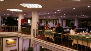 Vestíbulo de hotel con piano, zonas de estar y un techo decorativo.
