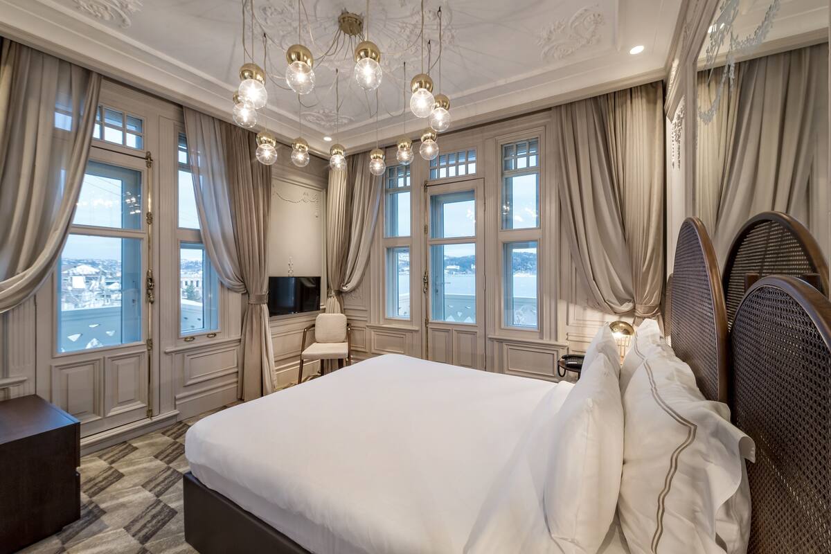 A spacious bedroom with a large bed, a television, and a view of the city through large windows.