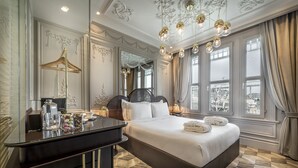 Een ruime slaapkamer met een groot bed, een kaptafel met spiegel en uitzicht op de stad door grote ramen.
