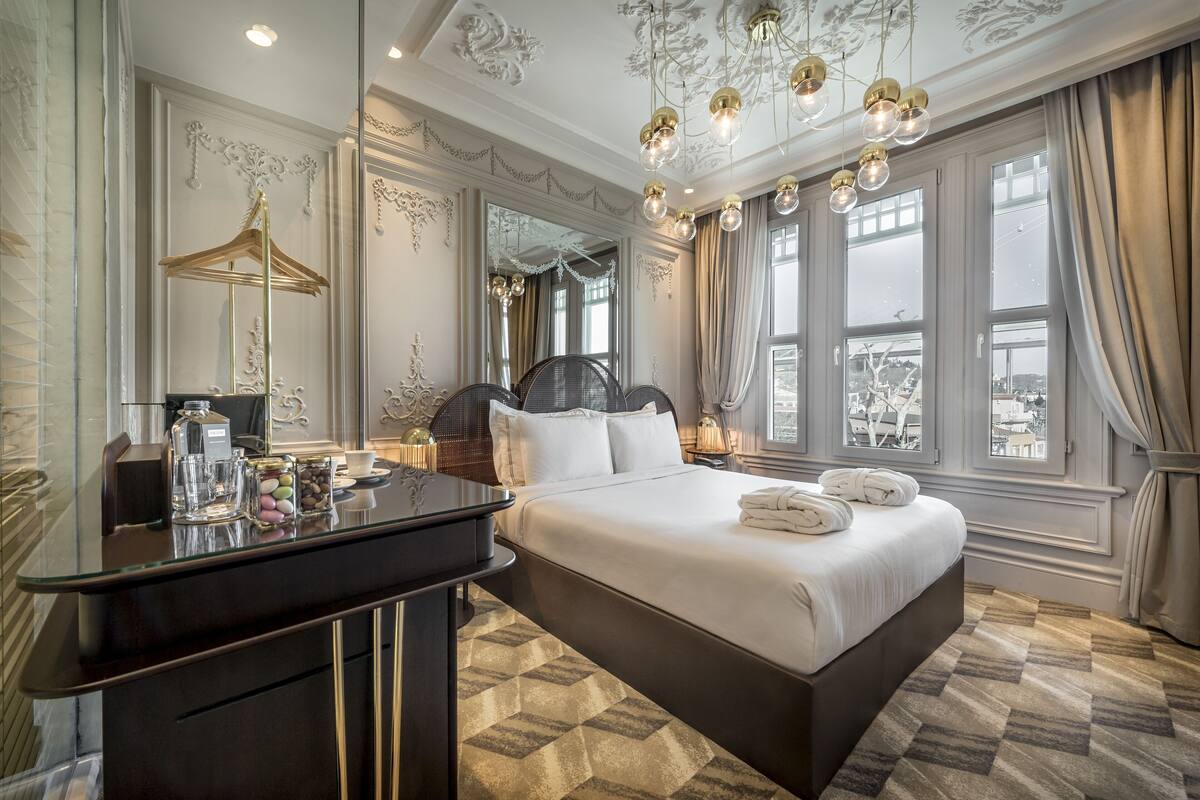 A spacious bedroom with a large bed, a vanity with a mirror, and a view of the city through large windows.