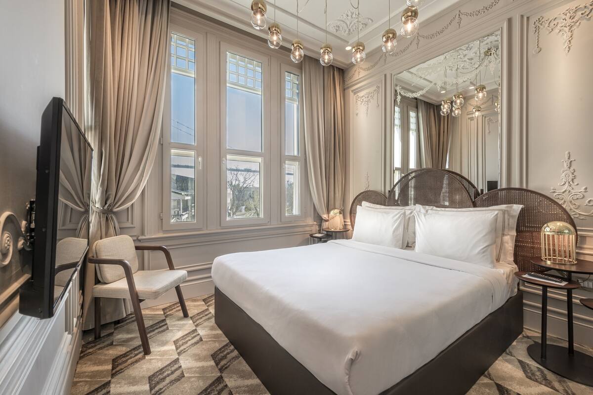 A large bed with a headboard, a chair, a bedside table, and a mirror.