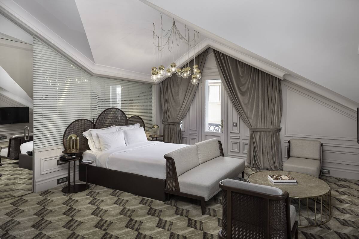 A modern hotel room with a large bed, a sofa, a small round table, and a TV.