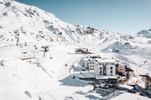 Una montaña cubierta de nieve con un telesilla, un edificio de varios pisos y una pista de esquí.