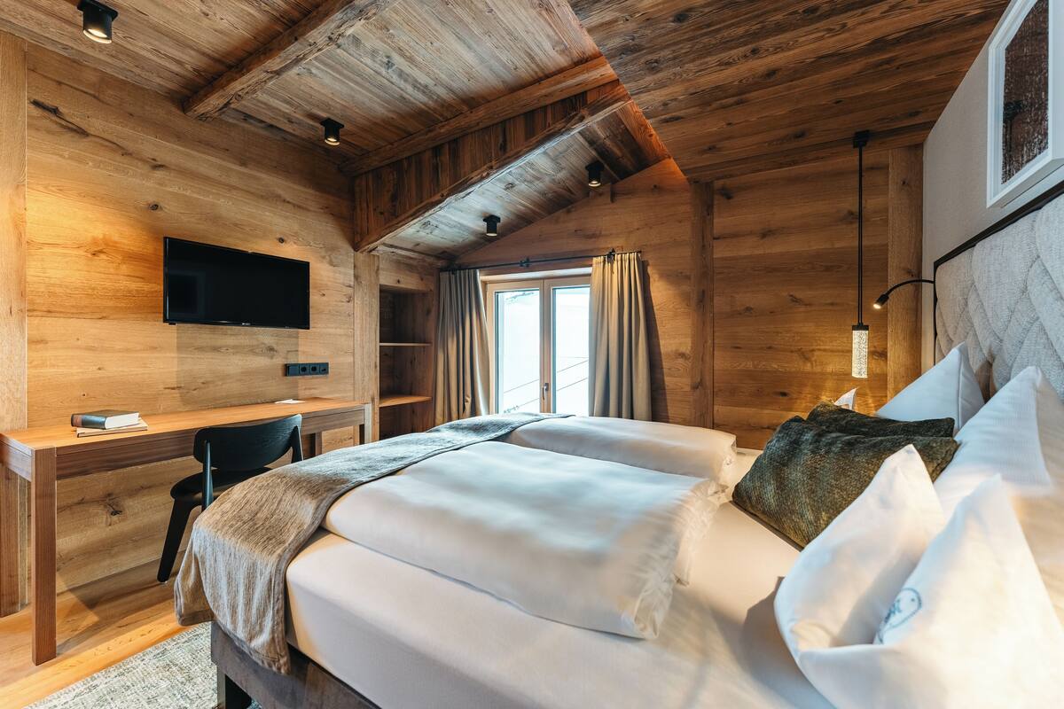 A wooden cabin bedroom with a bed, desk, and TV.