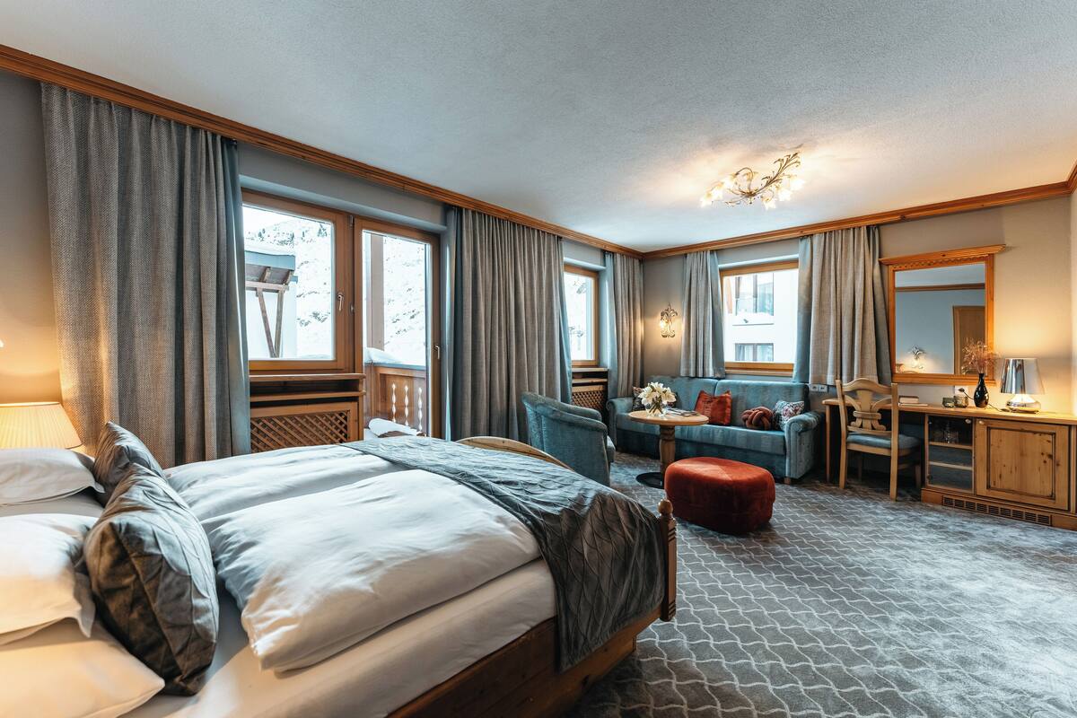A hotel room with a large bed, a desk, a chair, a sofa, and a small table with flowers.
