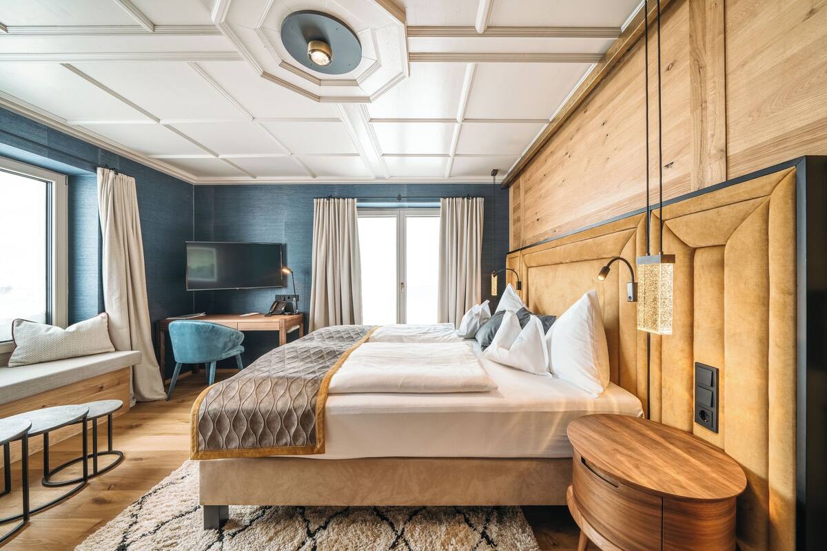 A modern hotel room with a large bed, a desk, a TV, and a view of the outdoors.