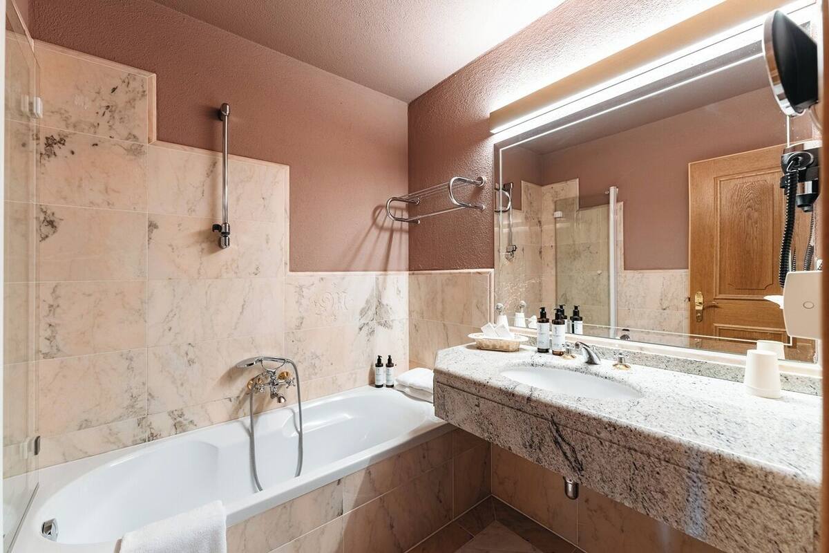 A modern bathroom with a bathtub, a large mirror, and a vanity with toiletries.