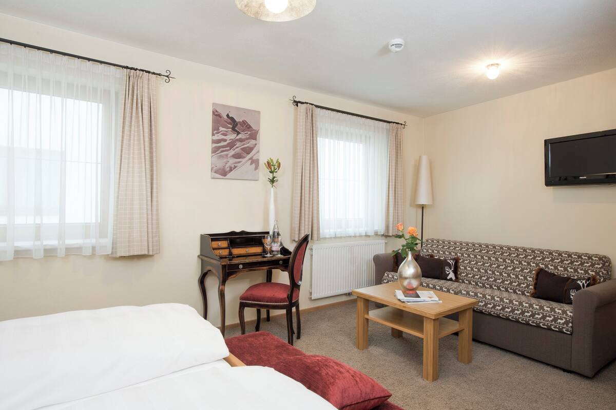 A hotel room with a bed, a desk, a chair, a sofa, a coffee table, and a TV.
