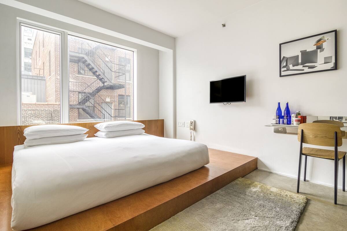 A modern bedroom with a large bed, a TV, and a city view.