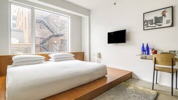 A modern bedroom with a large bed, a TV, and a city view.