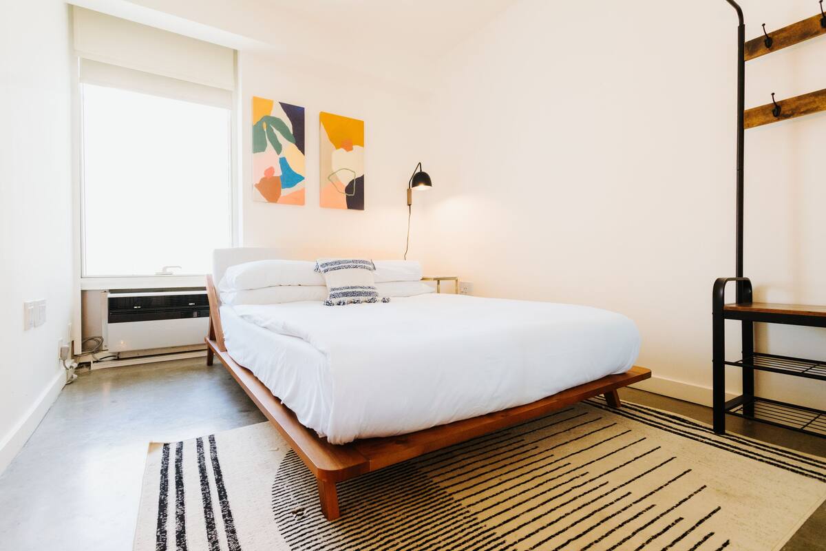 A bedroom with a bed, a desk, a lamp, and abstract wall art.