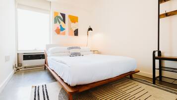 A bedroom with a wooden bed, white bedding, a black floor lamp, and abstract wall art.