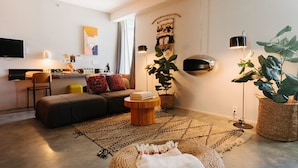 A modern living room with a sofa, ottoman, coffee table, and a flat-screen TV. - Hotel Alameda Highline (New York)