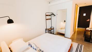A hotel room with a large bed, a bedside table, a mirror, a coat rack, and a desk with a chair.