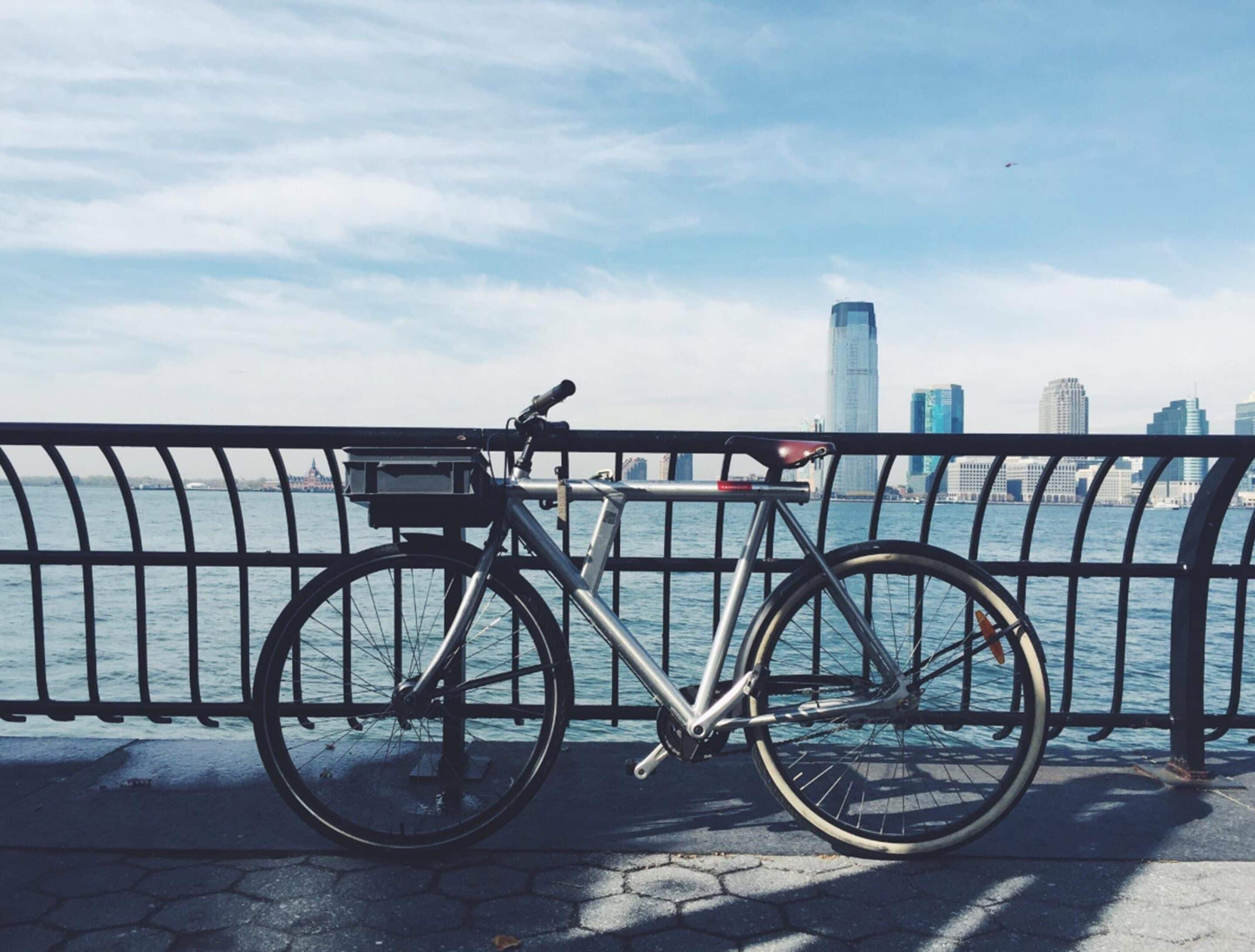 A bicycle parked by a waterfront with a city skyline in the background.