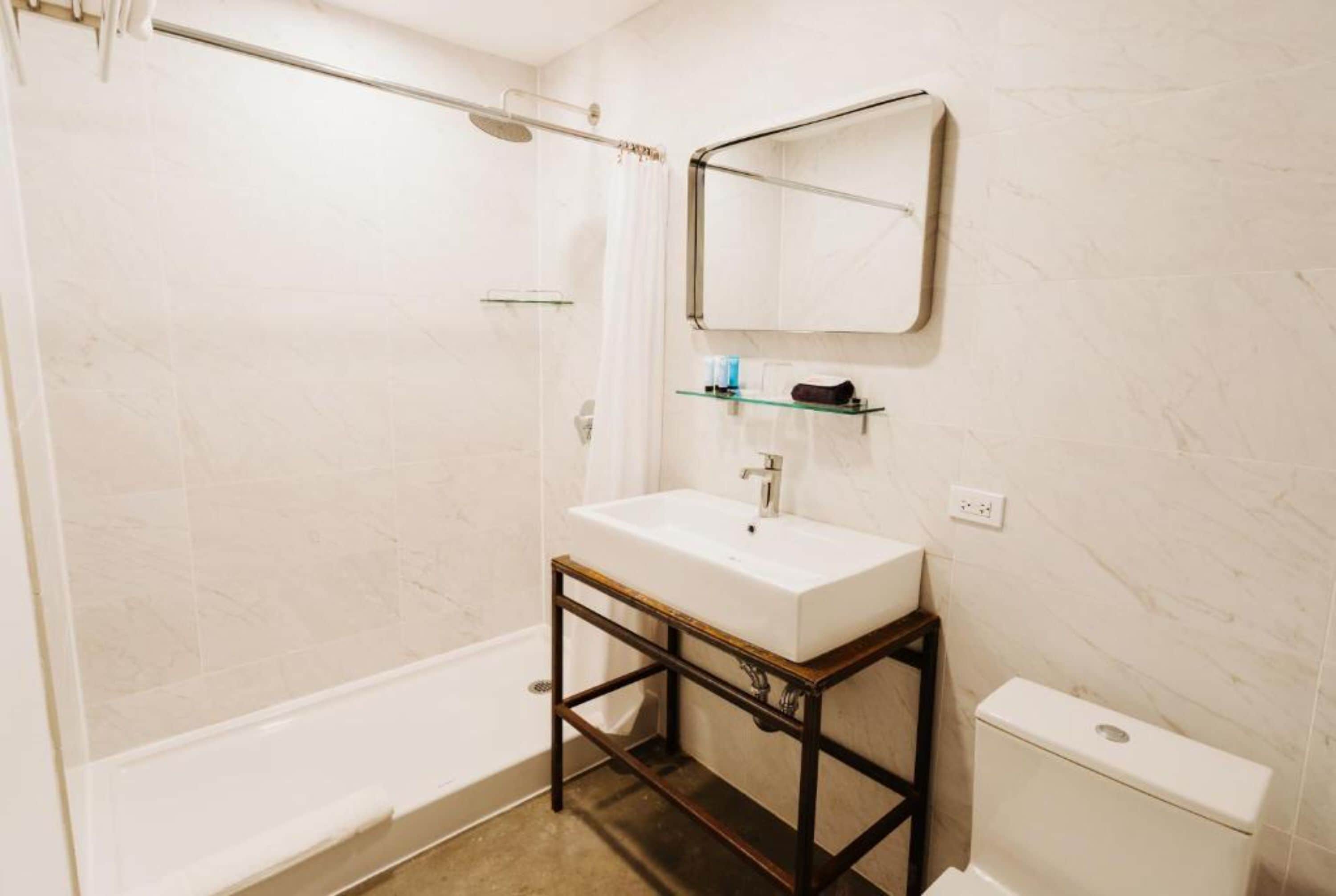 Une salle de bain avec un lavabo blanc, un miroir, une étagère en verre, une douche et des toilettes.