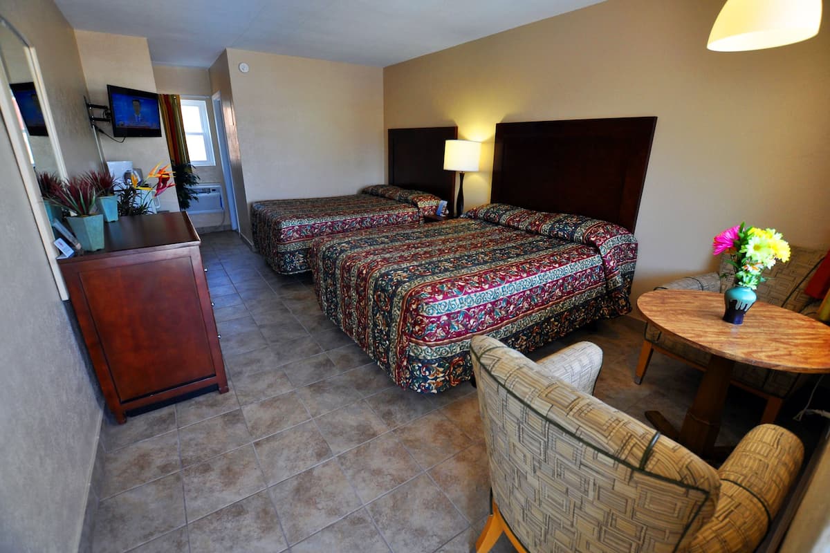 Une chambre d’hôtel avec deux lits, un bureau, une chaise, une petite table avec des fleurs et un téléviseur fixé au mur.