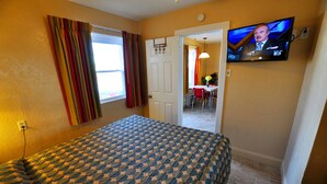 A hotel room with a bed, a television mounted on the wall, and a door leading to a dining area. - Nantucket Inn & Suites (Wildwood)