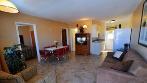 A living room with a sofa, a dining table with chairs, a TV, and a kitchen area with a refrigerator and cabinets. - Nantucket Inn & Suites (Wildwood)