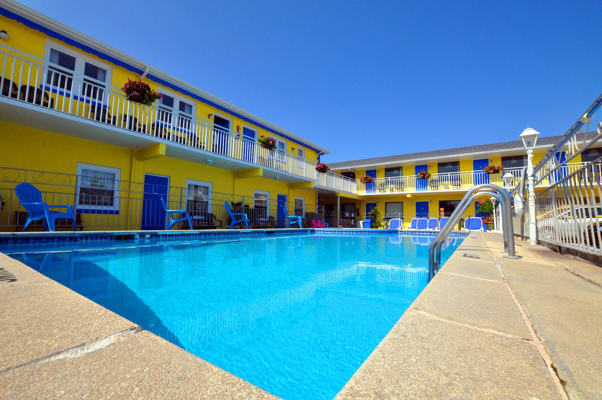 Ett hotell med en swimmingpool, blå stolar och gul- och blåfärgade ytterväggar.