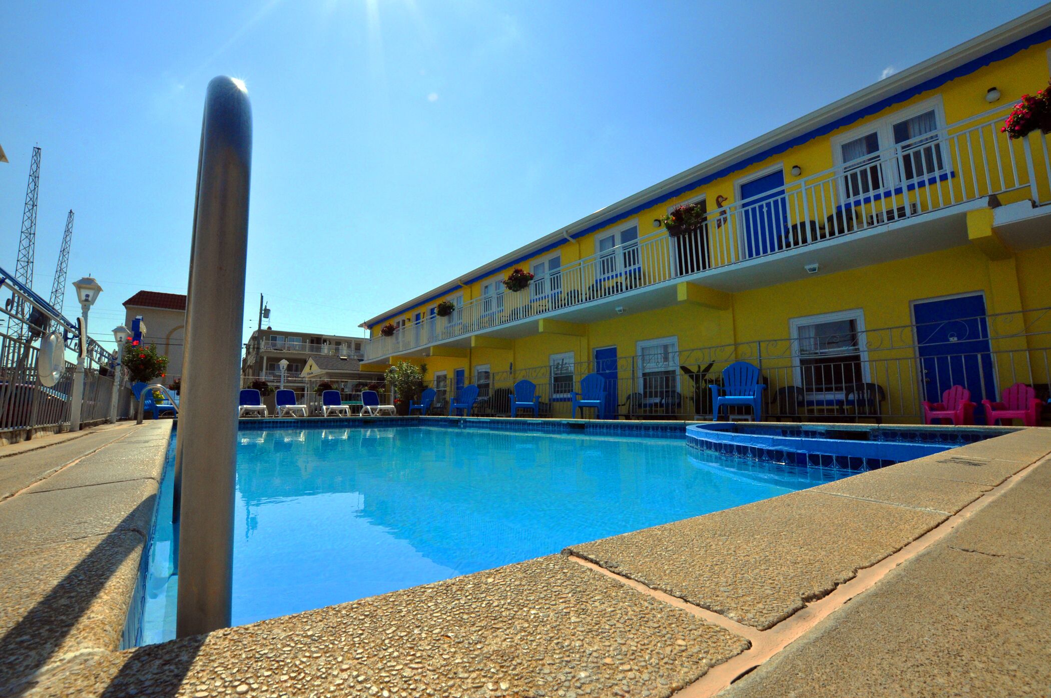 Piscina com cadeiras azuis e um edifício amarelo com varandas.
