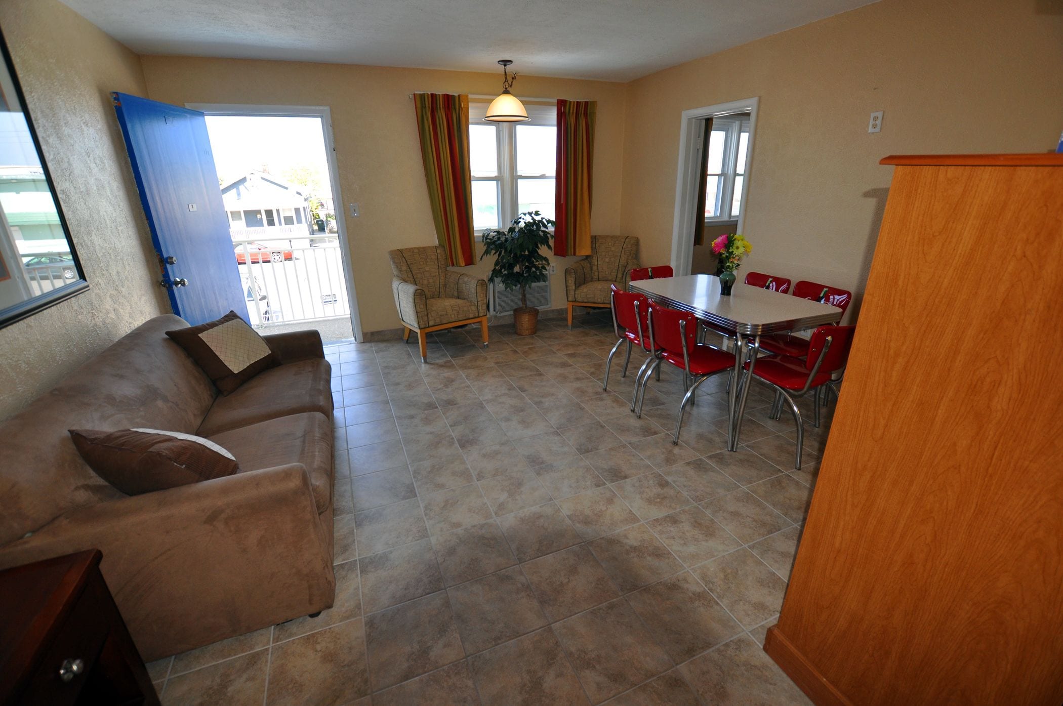 A living room with a sofa, a dining table with chairs, a potted plant, and a view of the outside.